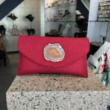 Sobre de fiesta rojo oscuro, tejido artesanalmente en la India, con cierre de solapa y broche magnético. Presenta un ágata central con borde dorado. Incluye asa de cadena dorada para llevar al hombro.