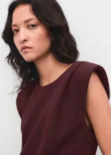 Blusa de color bordó con cuello barco, manga corta y hombreras marcadas que aportan estructura. Presenta un diseño recto y limpio con detalle de fruncido en los hombros.