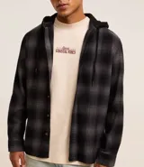 Camisa masculina de franela a cuadros en tonos grises y negros, con capucha con cordón ajustable, cierre frontal abotonado y mangas largas.