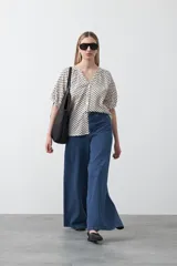 Camisa de viscosa con estampado de lunares pequeños en negro sobre fondo blanco o crema. Presenta escote en V con abertura y botones frontales, y mangas cortas abullonadas.