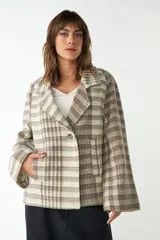 Saco corto de tela a cuadros color beige y marrón, con cuello solapa, manga larga y cierre frontal con un botón. Tiene un bolsillo de parche en el frente.