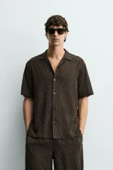 Camisa de corte relajado con cuello bowling y manga corta. Confeccionada en tejido fluido con textura jacquard de patrón geométrico y cierre frontal de botones.