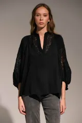 Camisa negra de corte holgado con cuello mao y escote en V. Presenta detalles de encaje en el cuello y en las mangas abullonadas de largo tres cuartos.