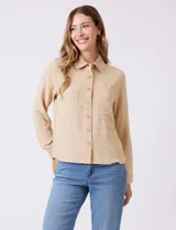 Camisa de crepe color beige con cuello clásico, cierre frontal con botones y dos bolsillos aplicados en el pecho.