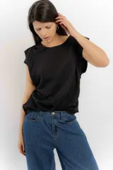 Remera sin mangas de corte holgado, con hombreras marcadas que crean un efecto de manga corta estructurada. Presenta un diseño minimalista con frunces laterales en la cintura y cuello redondo.