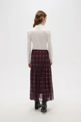 Falda larga de corte evasé con estampado de cuadros escoceses en tonos bordó y negro. Presenta un diseño de doble capa con una base opaca y una sobrecapa de tul semitransparente, con un corte asimétrico en la parte inferior.
