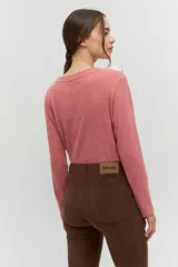 Remera de manga larga en tejido acanalado color rosa viejo, con un cuello redondo decorado con un volado amplio en color rosa claro que simula un collar.