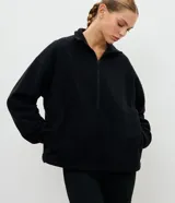Buzo deportivo de fleece color crema, con cuello alto y cierre frontal parcial. Presenta mangas largas con puños elásticos y un diseño holgado con recortes frontales.
