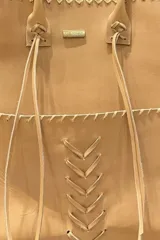 Matera artesanal confeccionada en cuero vacuno color tostado, con detalles de costuras a la vista y cordones decorativos entrelazados. Cuenta con placa metálica con la inscripción Uruguay.