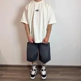 Remera negra de corte oversize con estampa rectangular en la espalda que representa una mano alcanzando un círculo sobre un fondo de líneas horizontales.