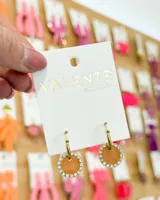 Aros colgantes dorados con forma circular, con borde de strass y centro color durazno.