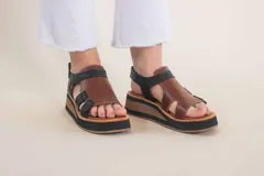 Sandalias de cuero color marrón con plataforma de madera y suela de goma negra. Tiras anchas de cuero marrón en el empeine y tobillo con ajuste de hebilla.