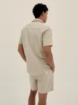 Conjunto de camisa de manga corta con cuello solapa y short con cordón ajustable, ambos en tejido ligero a rayas verticales celestes y blancas.