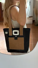 Bolso tote de ecocuero marrón oscuro con textura cocodrilo y un parche frontal de cuero liso marrón claro. Posee asas de hombro de cuero marrón y un broche decorativo blanco en el frente.