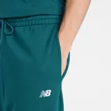 Pantalón de jogging New Balance color verde, con cintura elástica con cordón ajustable, puños elásticos en los tobillos y logo de la marca bordado en la pierna izquierda.
