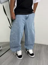 Pantalón de jean estilo baggy, color azul claro, con diseño de llamas bordadas en el lateral de la pierna derecha.