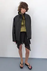 Cazadora de corte oversize confeccionada en 100% piel. Presenta cuello subido, manga larga con hombro caído y cierre frontal mediante cremallera y botones a presión ocultos bajo una solapa. Incluye bolsillos laterales ocultos en las costuras y forro interior.
