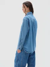 Camisa de denim de corte recto y estilo clásico, confeccionada en tejido de algodón con acabado lavado. Presenta cuello camisero, cierre frontal con botones metálicos y mangas largas con puños abotonados.