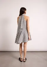 Vestido corto blanco con lunares negros, cuello halter y corte evasé.