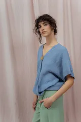 Blusa de lino color fucsia, con escote en V y manga corta amplia. Presenta un detalle de botón decorativo dorado en el centro del escote.