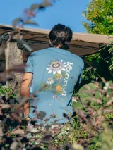 Remera de algodón blanca con cuello redondo y manga corta, presenta un pequeño estampado de un fruto de mburucuyá en el lado izquierdo del pecho.