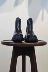Bota tipo Chelsea de caña corta en color beige, confeccionada en material sintético con acabado liso. Presenta paneles elásticos laterales a tono y una suela track robusta y dentada que aporta altura y estilo moderno.