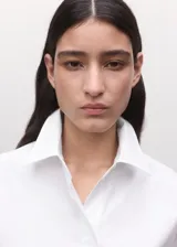 Camisa blanca de algodón con diseño recto, cuello camisero, manga corta y cierre frontal de botones ocultos con tapeta.