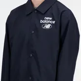 Campera tipo coach jacket New Balance, color negro, con cuello camisero, cierre frontal con botones a presión y logo estampado en el pecho. Confeccionada en tejido ligero de poliéster reciclado con ajuste holgado.