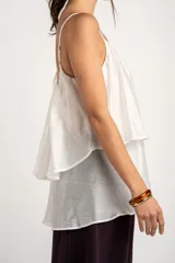 Top de tirantes blancos con diseño fluido y volado superpuesto en el pecho.