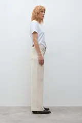 Jean de corte wide leg en color beige claro, con tiro medio y cierre frontal con botón y cremallera. Presenta un diseño de cinco bolsillos y costuras reforzadas.