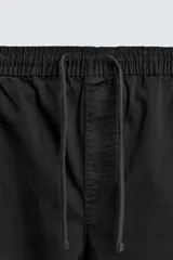 Pantalón cargo de corte slim fit en color negro, confeccionado en tejido de algodón con elasticidad. Presenta cintura elástica ajustable con cordón, bolsillos laterales tipo cargo con solapa y bajo acabado en puño elástico.