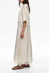 Vestido largo color crudo de manga corta, con inserciones de encaje transparente en forma de V en el pecho y detalles de encaje en el dobladillo inferior.