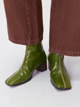 Botas de caña media color marrón, confeccionadas en cuero con acabado brillante. Presentan punta cuadrada, taco de madera y un distintivo bordado decorativo en color rojo que recorre el empeine hasta la punta.