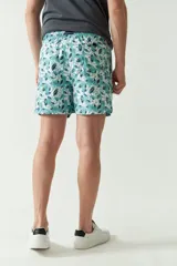 Short de baño con estampado botánico en tonos turquesa, blanco y azul. Presenta cintura elástica con cordón ajustable, dos bolsillos laterales y uno trasero, además de un logo bordado en la pierna.