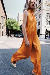 Mono largo satinado color naranja, de corte amplio con pierna ancha, cuello redondo y manga sisa, con detalle de tejido arrugado y cierre en la espalda.