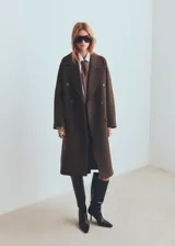 Abrigo de corte sastre con diseño de doble botonadura y solapas amplias. Presenta un estampado de cuadros pequeños en tonos marrones y oscuros, con una silueta estructurada y elegante.