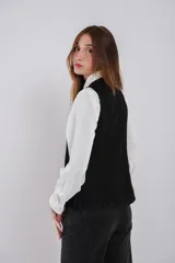 Chaleco entallado de jean negro con cuello a la base, cierre frontal con botones, bolsillos simulados y abertura en la parte trasera.