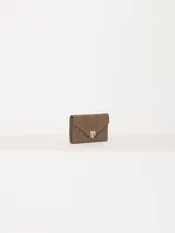 Billetera de cuero vacuno con textura graneada en color marrón. Presenta un diseño tipo sobre con cierre magnético y un aplique metálico distintivo en forma de llama en la parte frontal.