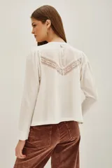 Camisa de manga larga color negro, con cuello redondo y cierre frontal de botones. Presenta un diseño con volados en la parte superior delantera y detalles de encaje bordado en los hombros y pecho.