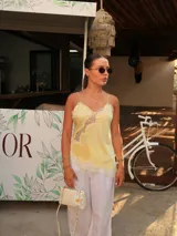 Blusa de satén color amarillo suave, estilo camisola, con delicados detalles de encaje blanco en el escote y el dobladillo, breteles finos y silueta fluida.