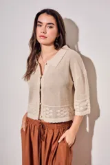 Cardigan de algodón peinado color beige, con cuello camisero, cierre frontal de botones y detalles de textura en crochet con diseño de flores. Mangas tres cuartos y diseño corto.