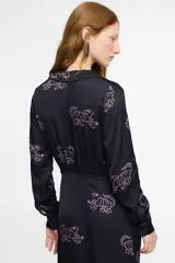 Vestido largo estilo camisero confeccionado en seda viscosa color negro con estampado de tigres en color rosa. Tiene cuello camisero, mangas largas, corte cruzado y lazo en la cintura.