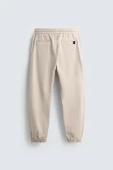Pantalón tipo jogger de corte slim fit, confeccionado en tejido de algodón con elasticidad. Presenta cintura elástica ajustable con cordón, bolsillos frontales, bolsillos traseros de vivo y bajos con puños elásticos.