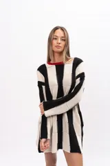 Buzo tipo poncho de corte oversize y holgado, con diseño de bloques verticales en colores blanco y negro. Presenta cuello redondo con detalle en color rojo, mangas largas y bolsillos laterales.