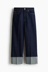 Jean de denim azul oscuro rígido, con diseño de pierna amplia y tiro alto. Presenta bolsillos, pinzas delanteras y traseras, y un dobladillo ancho vuelto hacia arriba en los tobillos.