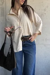 Camisa beige de manga larga con detalles bordados en la botonera y el cuello, cierre frontal con botones y diseño fluido.