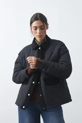 Campera tipo barn capitoneada de color marrón, con silueta corta y relajada. Presenta cuello de pana, cierre frontal con broches metálicos y bolsillos laterales funcionales.