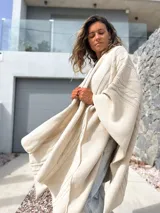 Ruana tejida en color crudo con diseño de trenzas y textura en relieve. Presenta un corte amplio y envolvente, ideal para usar como capa sobre otras prendas.