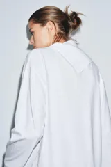 Camiseta blanca de manga larga con cuello redondo y superposición de tela tipo pañuelo.