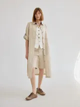 Vestido camisero midi de lino color beige, con diseño de manga corta con solapa, cuello camisero, bolsillo trasero con solapa y botón, y aberturas laterales en el ruedo.